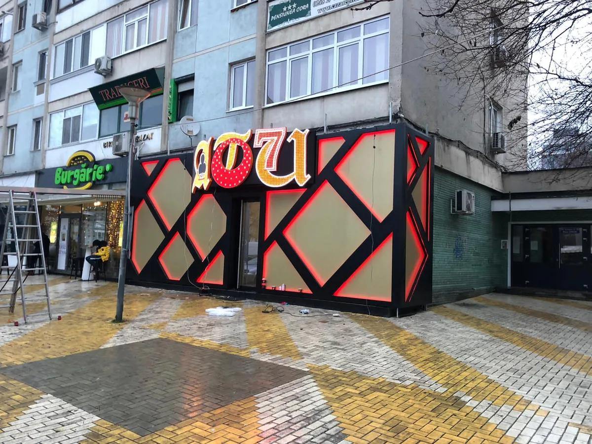 Fațadă neagră cu model romboidal roșu și siglă luminoasă, montată pe structură metalică — Lartek Grup